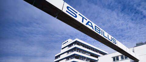 Firmengebäude der Stabilus Gruppe mit modernem Architekturdesign und einer markanten Brücke mit dem Schriftzug „STABILUS“ vor blauem Himmel.