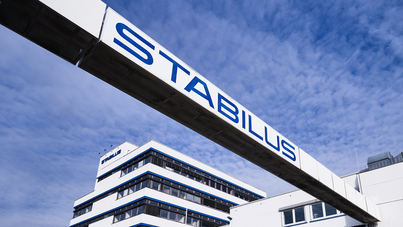 Firmengebäude der Stabilus Gruppe mit modernem Architekturdesign und einer markanten Brücke mit dem Schriftzug „STABILUS“ vor blauem Himmel.