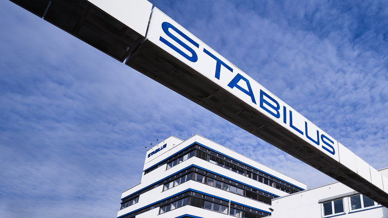 Firmengebäude der Stabilus Gruppe mit modernem Architekturdesign und einer markanten Brücke mit dem Schriftzug „STABILUS“ vor blauem Himmel.