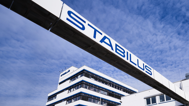 Firmengebäude der Stabilus Gruppe mit modernem Architekturdesign und einer markanten Brücke mit dem Schriftzug „STABILUS“ vor blauem Himmel.